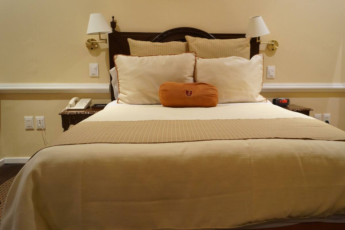 Une chambre d’hôtel avec un lit, deux lampes de chevet, une table de chevet avec un téléphone et une horloge.