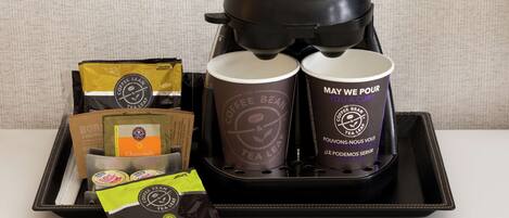 A coffee maker, two coffee cups, a tea bag, and a packet of coffee beans on a tray.
