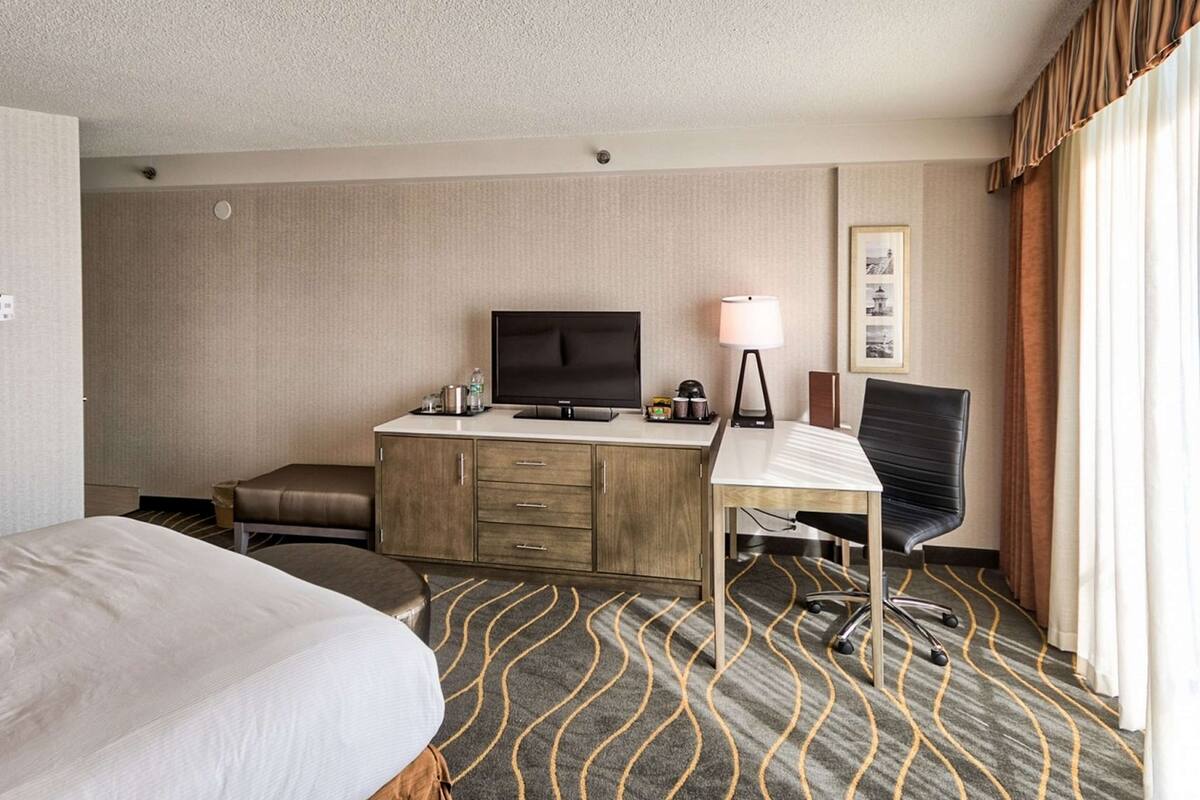 A hotel room with a bed, a desk with a computer, a chair, a television, and a lamp.
