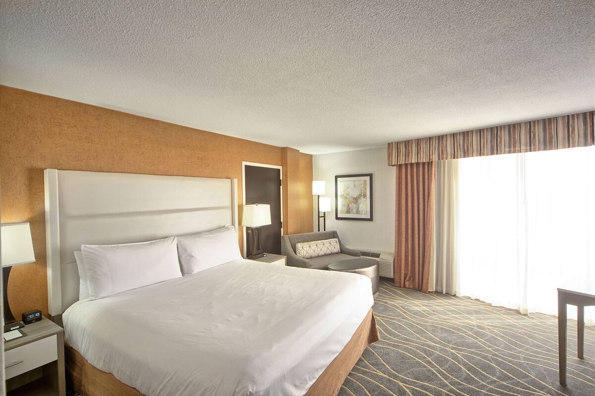 A hotel room with a large bed, a desk, a chair, and a small table.