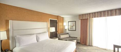 A hotel room with a large bed, a desk, a chair, and a small table.