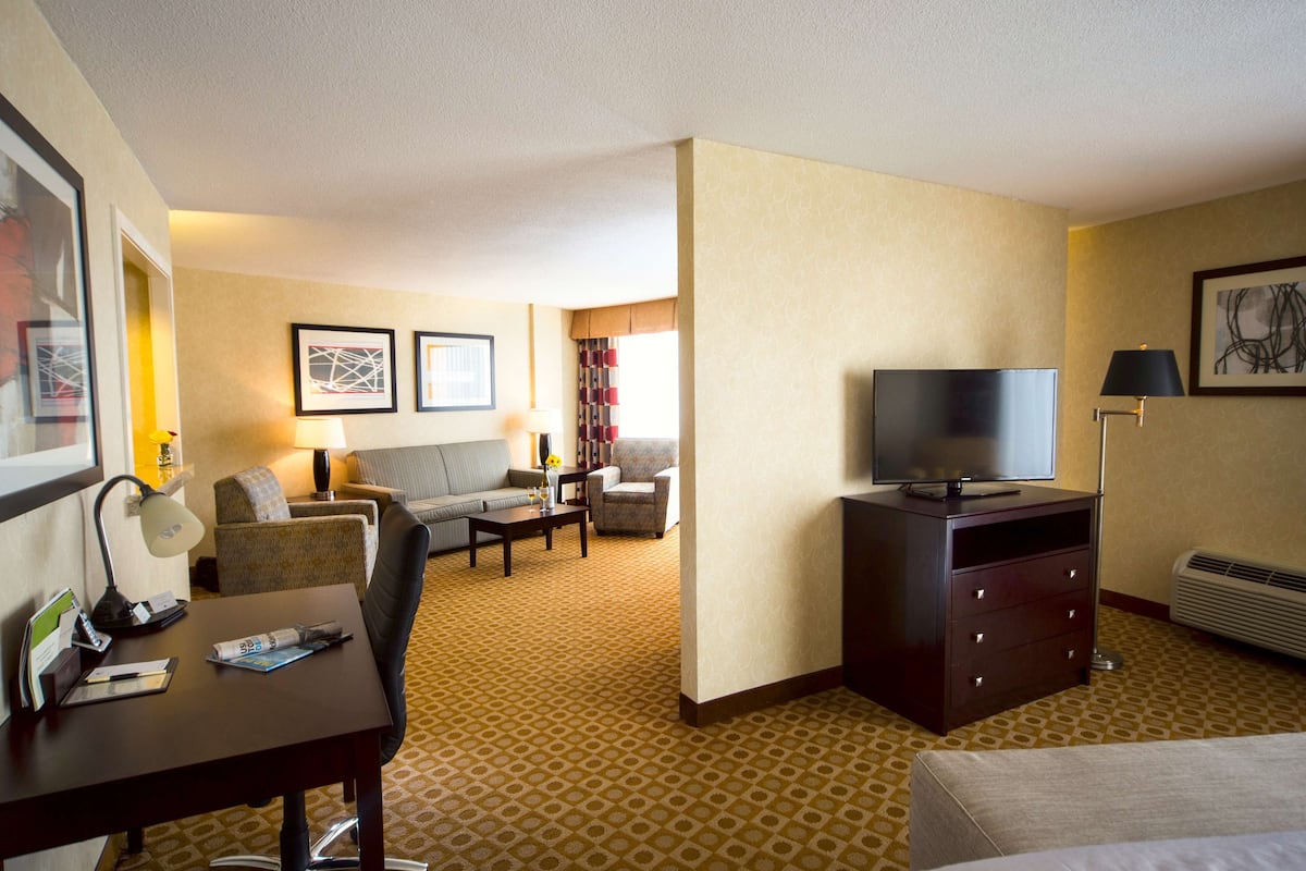 A hotel room with a bed, a desk with a lamp, a TV, a sofa, and a coffee table.