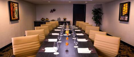 A conference room with a long table, beige chairs, and a dark wooden table.