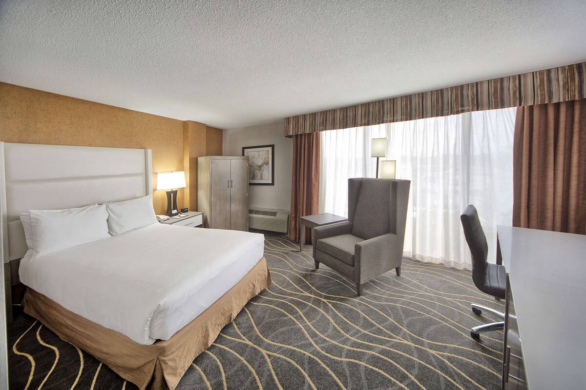 A hotel room with a large bed, a desk, a chair, a wardrobe, and a window with curtains.