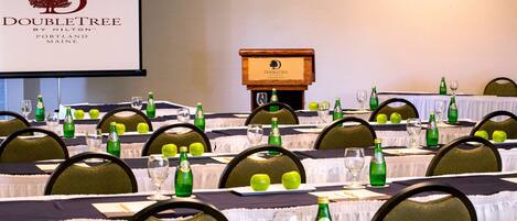 A conference room with tables set for a meeting, each with green bottles, glasses, and apples. A podium with the DoubleTree logo is visible in the background.