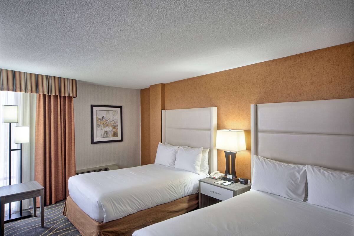 A hotel room with two beds, a desk, a lamp, and a framed picture on the wall.