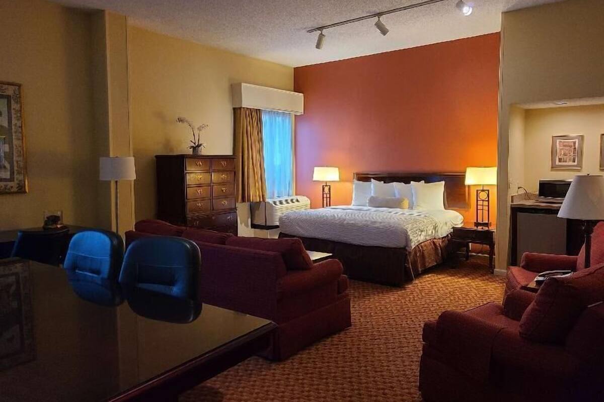 A hotel room with a bed, two armchairs, a desk, and a dresser.