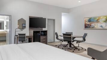 Habitación de hotel moderna con una cama grande, un escritorio con televisor de pantalla plana, microondas y zona de estar con sillas.
