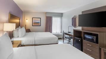 A hotel room with two beds, a desk, a flat-screen TV, a microwave, and a window with curtains.
