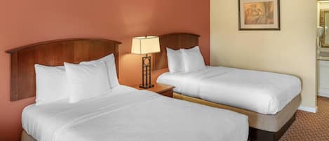 A hotel room with two beds, a nightstand with a lamp, a painting on the wall, and a bathroom visible to the right.
