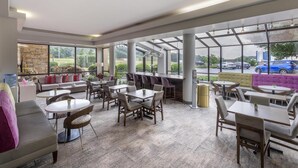A spacious indoor area with multiple seating arrangements, including tables and chairs, and large windows offering views of the outside. - Best Western Hickory (Hickory)