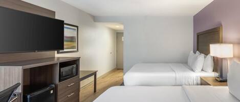 A hotel room with a flat-screen TV, a microwave, a refrigerator, a bed with white linens, and a bedside table with a lamp.