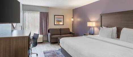 A modern hotel room with a large bed, a desk, a sofa, and a TV.
