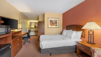 Habitación de hotel con cama, escritorio, silla, televisión y lámpara.