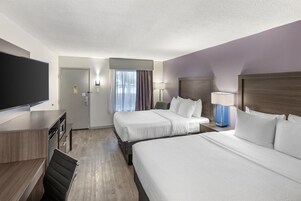 A hotel room with two beds, a desk, a TV, and a bathroom.
