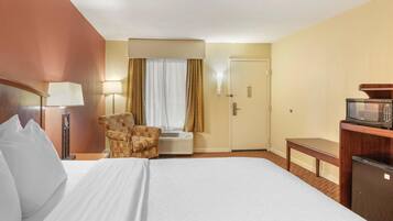 Habitación de hotel con cama, una silla, escritorio, microondas y puerta.