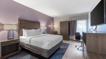 A hotel room with a large bed, a desk with a chair, a flat-screen TV, and a wardrobe.
