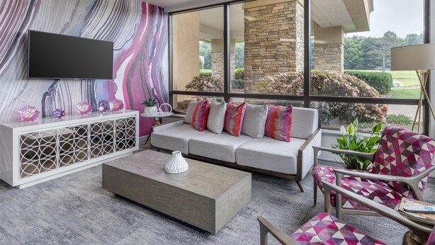 A modern living room with a large window, a white sofa, a coffee table, and a TV mounted on the wall. - Best Western Hickory (Hickory)