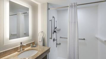 A bathroom with a granite countertop sink, a mirror, a shower with a glass door, and a white tiled wall.