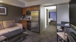Una habitación de hotel compacta con kitchenette, un sofá, una pequeña mesa de comedor y un televisor de pantalla plana.