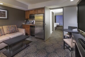 A compact hotel room with a kitchenette, a sofa, a small dining table, and a flat-screen TV. - Holiday Inn & Suites Phoenix Airport North by IHG (Phoenix)
