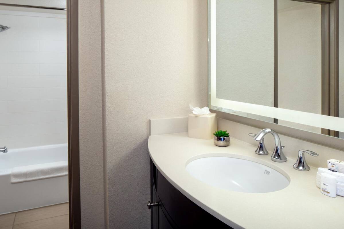 A bathroom with a bathtub, a sink, a mirror, and toiletries.