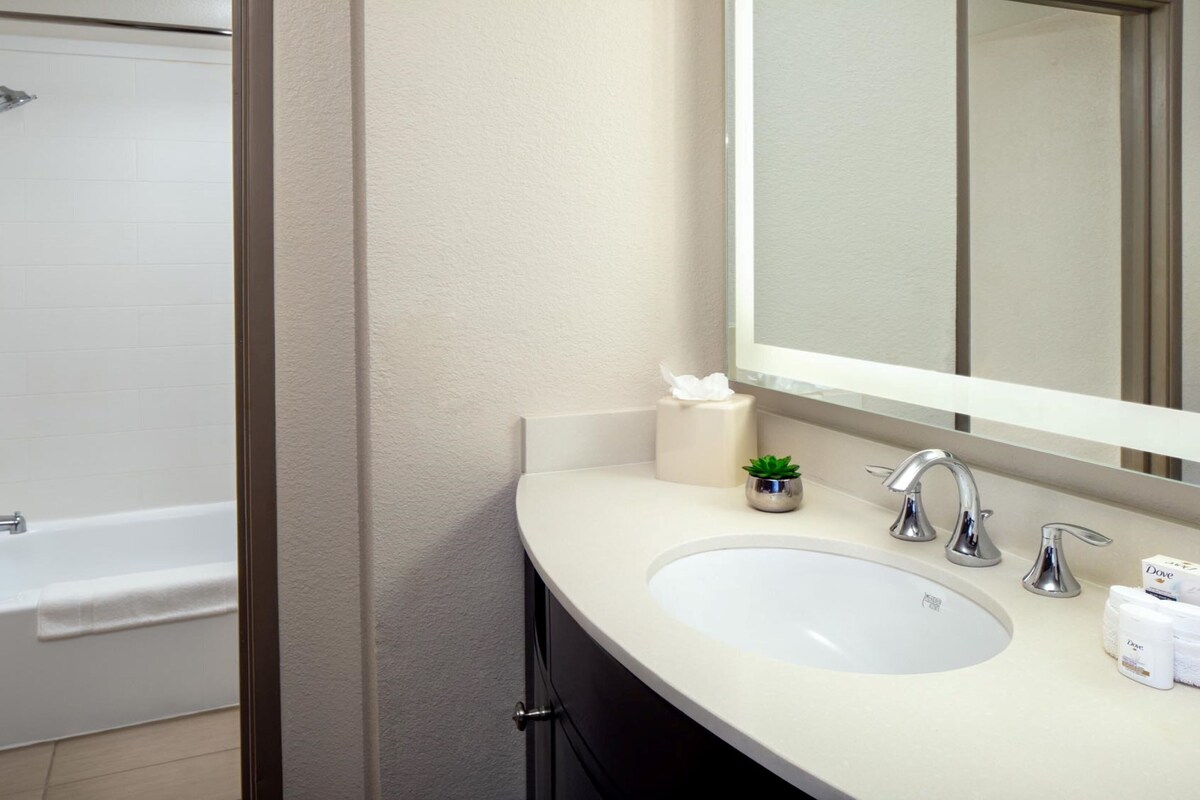 A bathroom with a bathtub, a sink, a mirror, and toiletries.