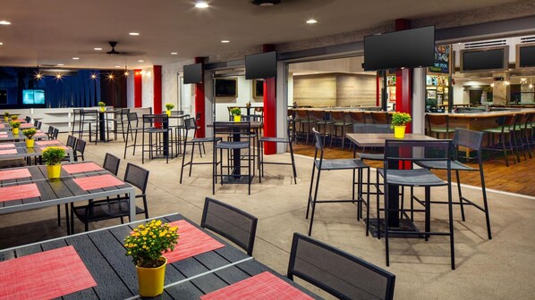 A spacious indoor dining area with multiple tables and chairs, a bar area, and a television screen mounted on the wall. - Holiday Inn & Suites Phoenix Airport North by IHG (Phoenix)