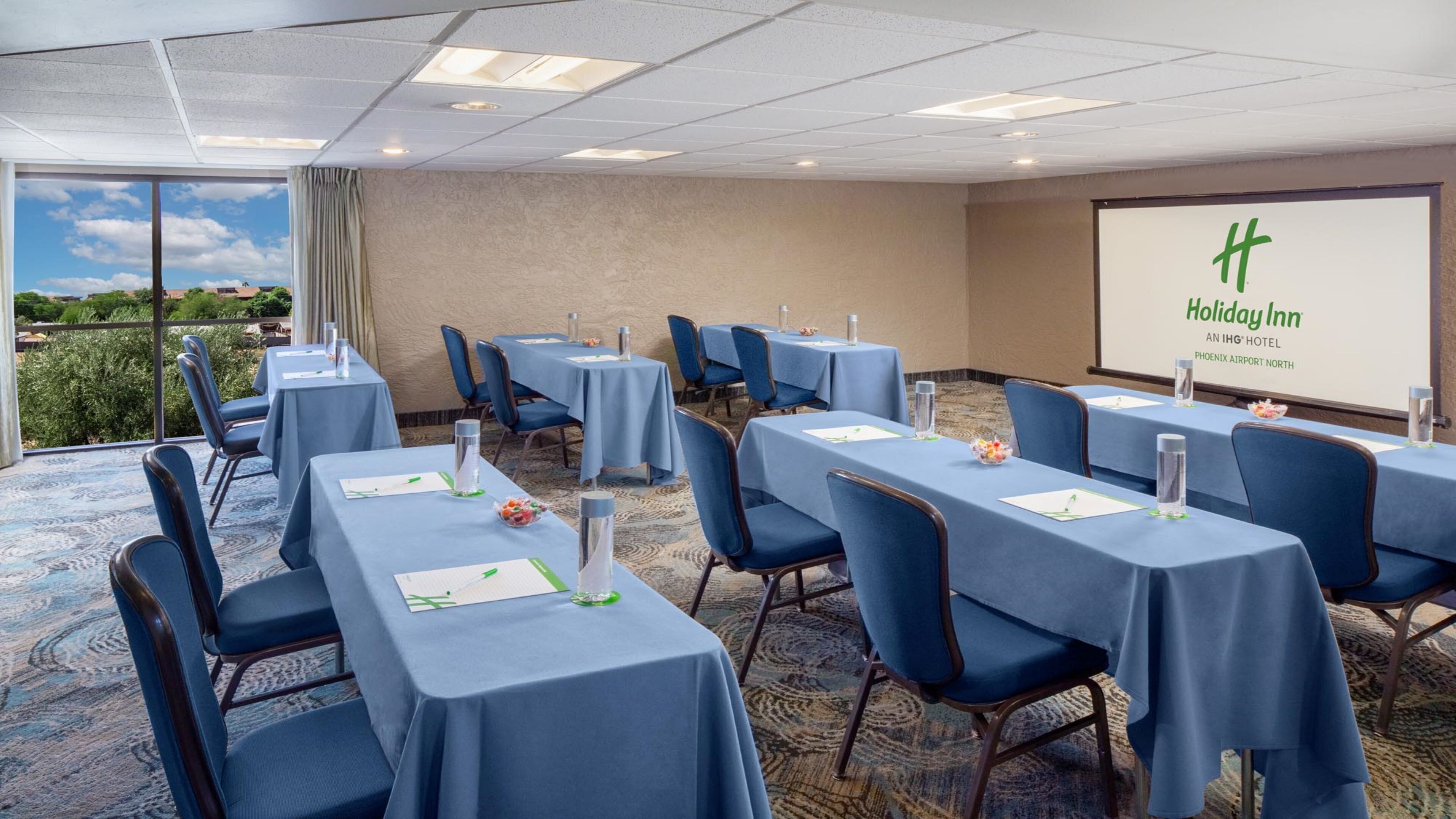 Una sala conferenze con tavoli, sedie e uno schermo per presentazioni all'Holiday Inn Phoenix Airport North.
