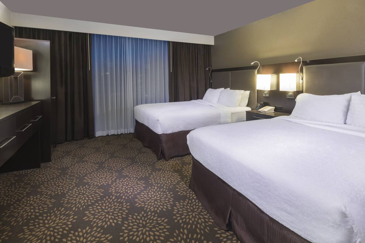 A hotel room with two beds, a desk, a TV, and a nightstand.
