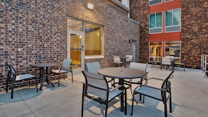 An outdoor patio with brick walls, metal furniture, and a glass door leading to an interior space.