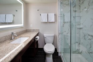 A bathroom with a granite countertop, a white toilet, and a glass shower enclosure.