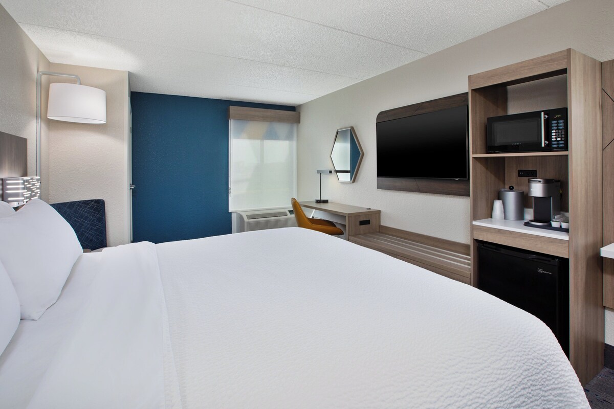 A hotel room with a large bed, a desk with a chair, a television, a microwave, and a coffee maker.