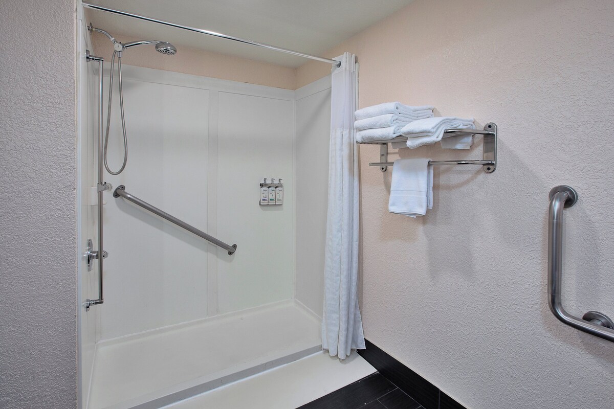 A shower with a glass door, a grab bar, and a towel rack with folded towels.