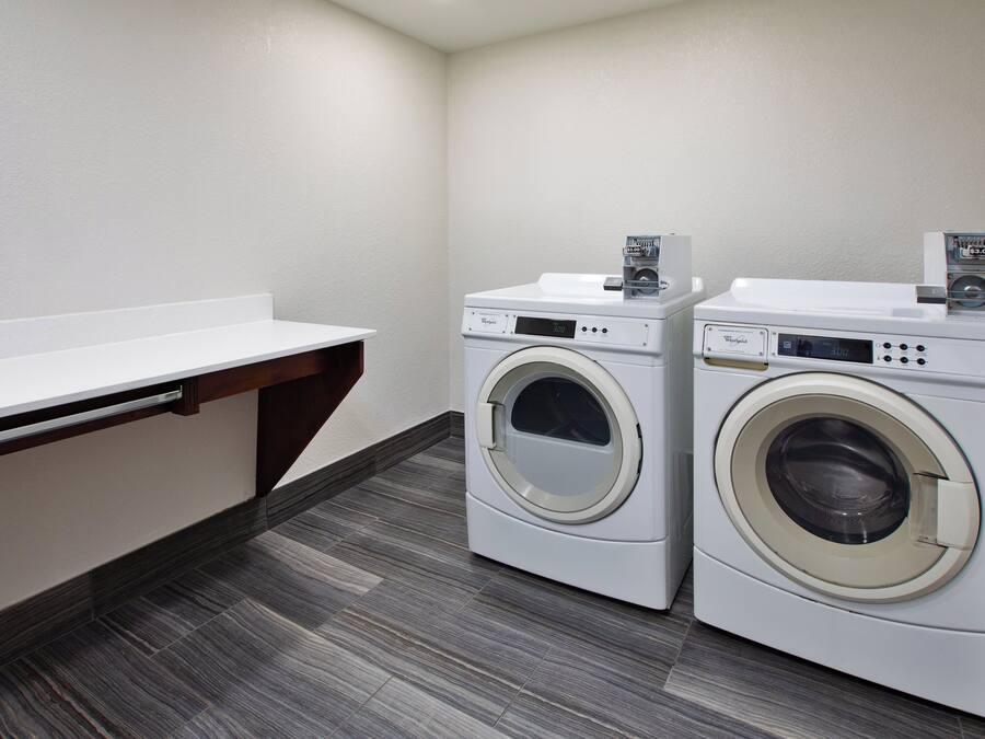 A laundry room with two front-loading Whirlpool washers, a white countertop, and a dark wood floor.