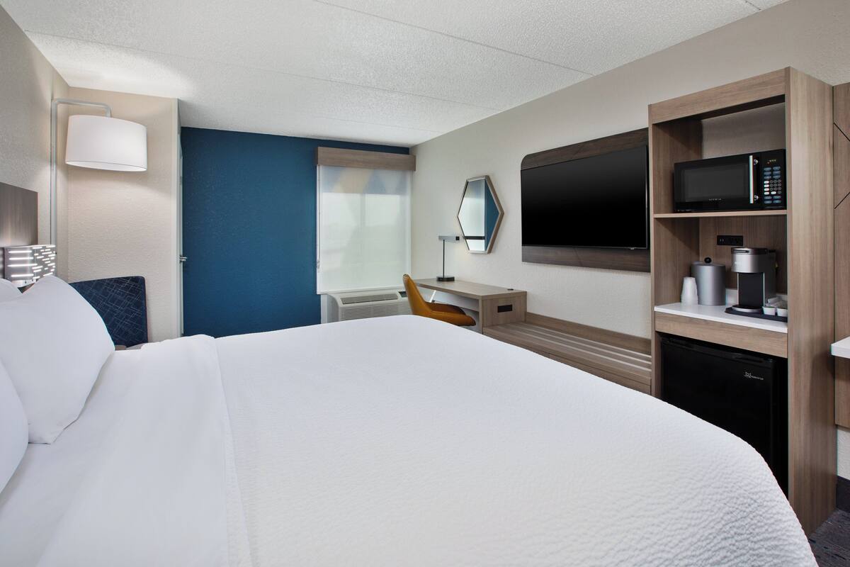 A hotel room with a large bed, a desk with a chair, a television, a microwave, and a coffee maker.
