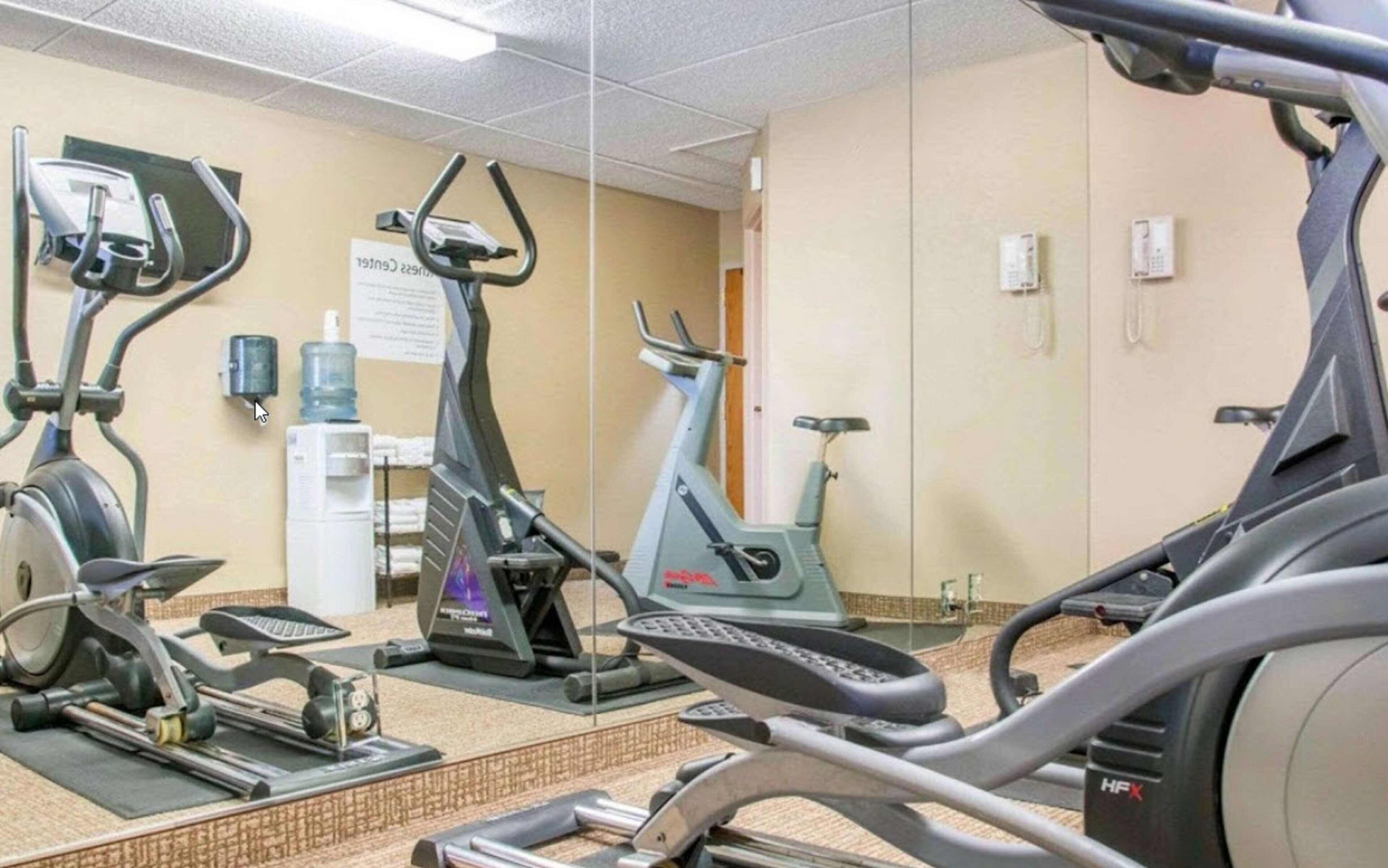 Un gimnasio con bicicletas estáticas, elípticas y un dispensador de agua.