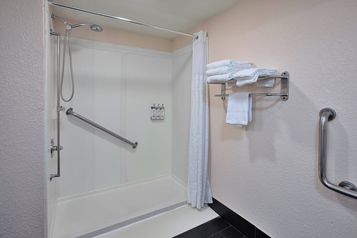 A shower with a glass door, a grab bar, and a towel rack with folded towels.