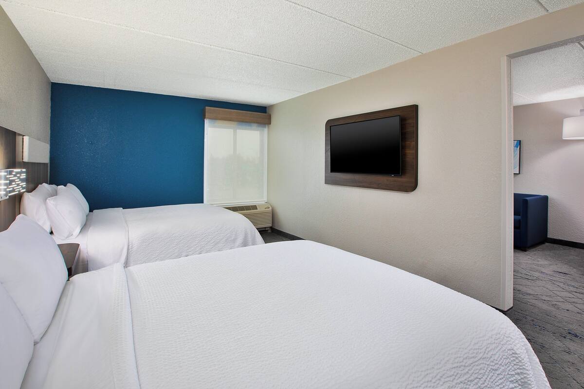 A hotel room with two beds, a flat-screen TV, and a window with blinds.