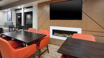 A modern conference room with a large table, orange upholstered chairs, a flat-screen TV mounted on the wall, and a built-in fireplace.