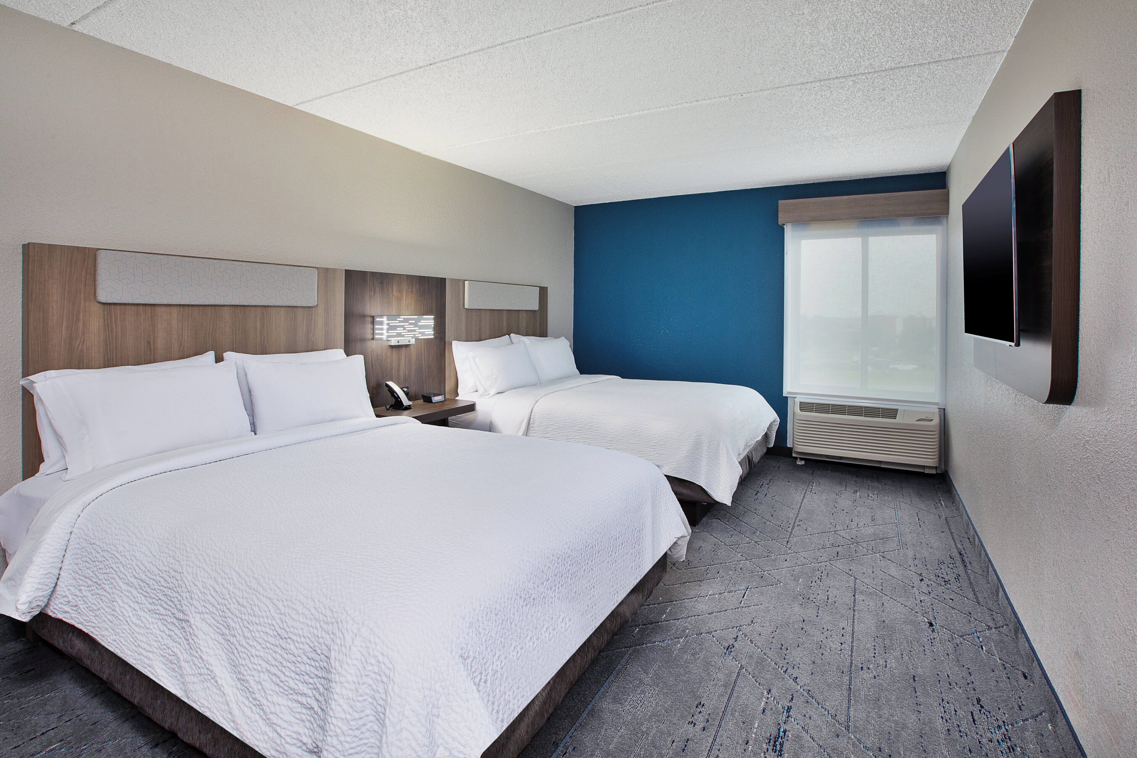 Une chambre d’hôtel avec deux lits, une grande fenêtre, un téléviseur à écran plat et un système de climatisation intégré.
