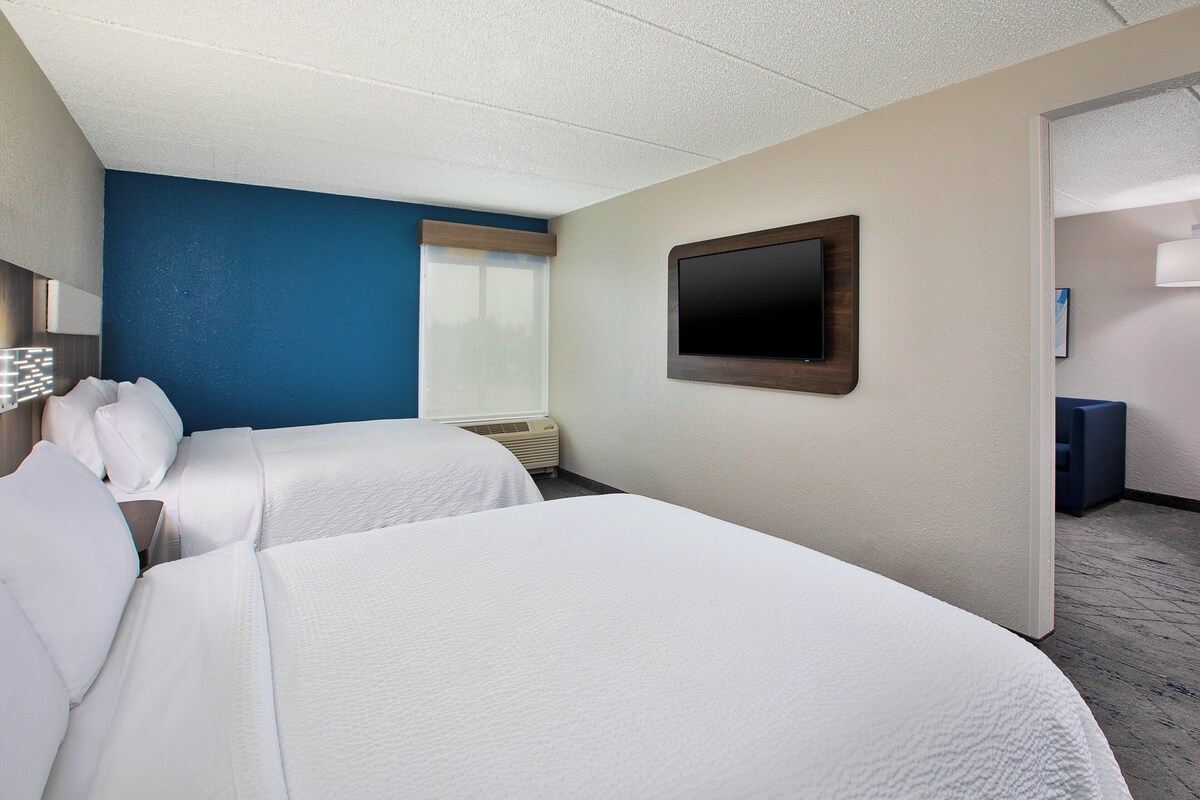 A hotel room with two beds, a flat-screen TV, and a window with blinds.