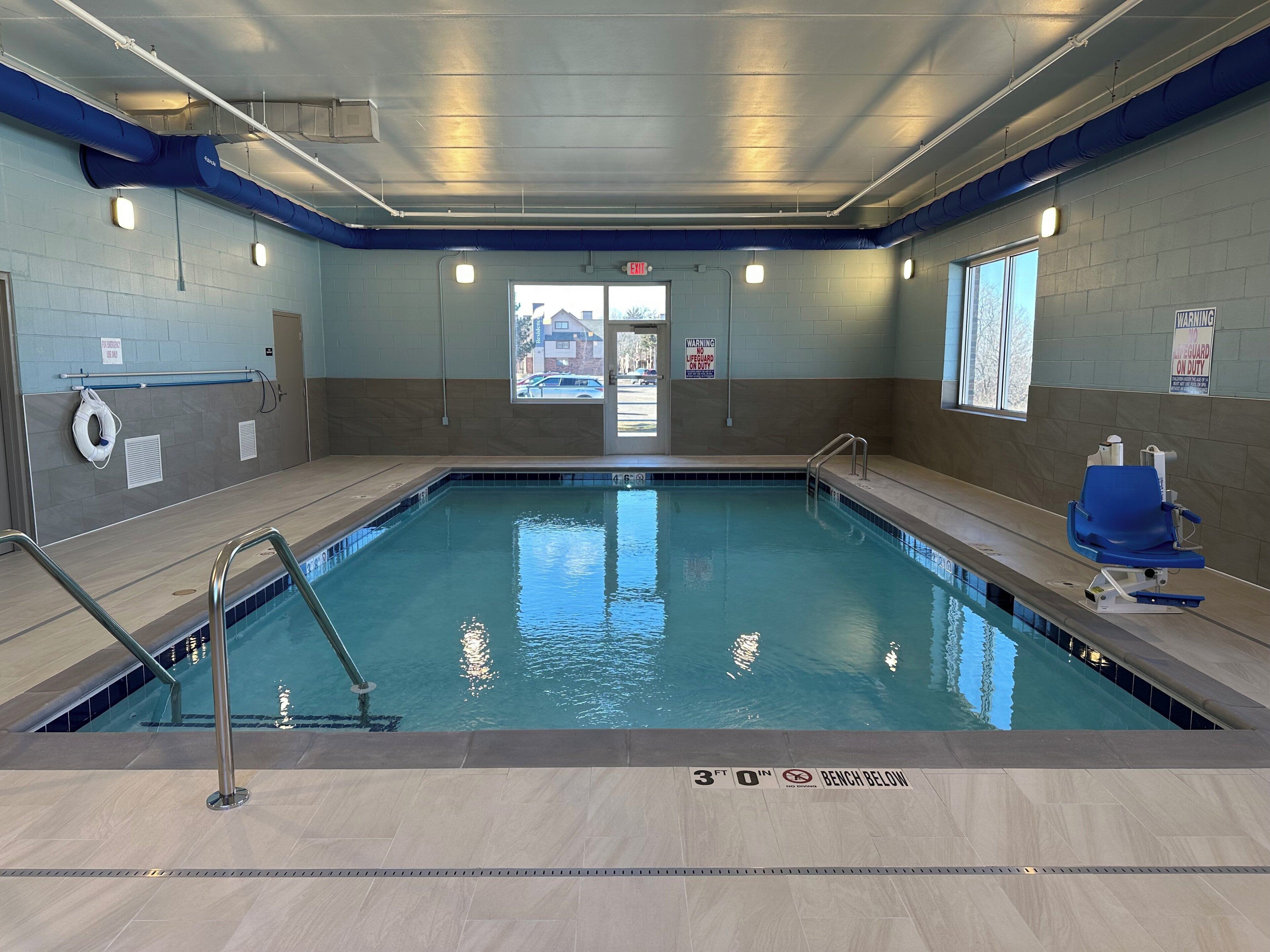 Una piscina interior con agua cristalina, una silla de socorrista y un banco.