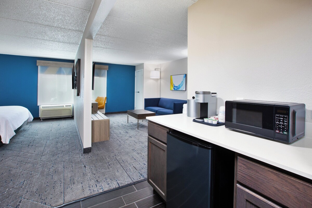 A hotel room with a bed, a sofa, a small table, a microwave, and a coffee maker.
