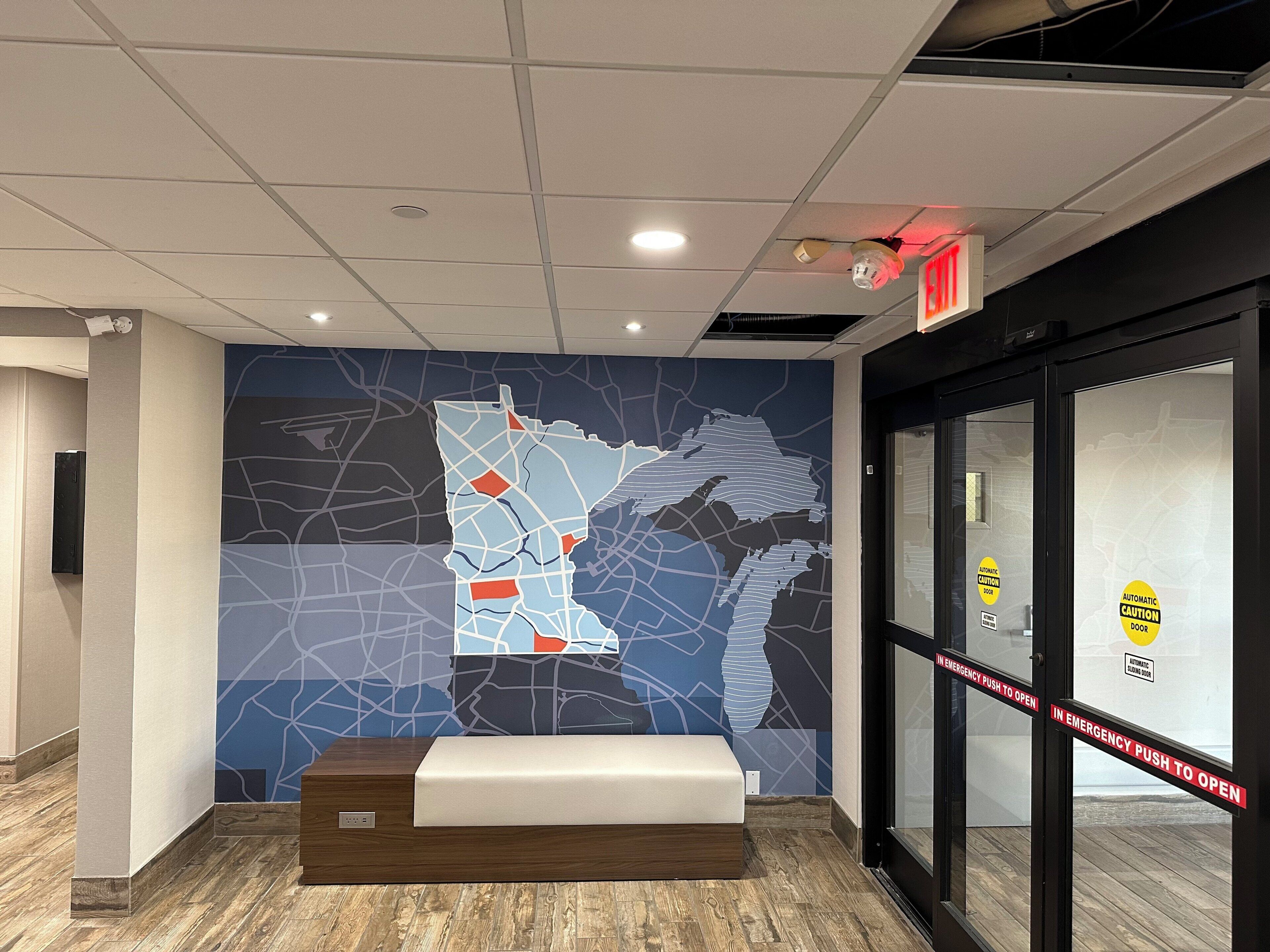 A lobby with a map mural, a reception desk, and emergency exit signs.