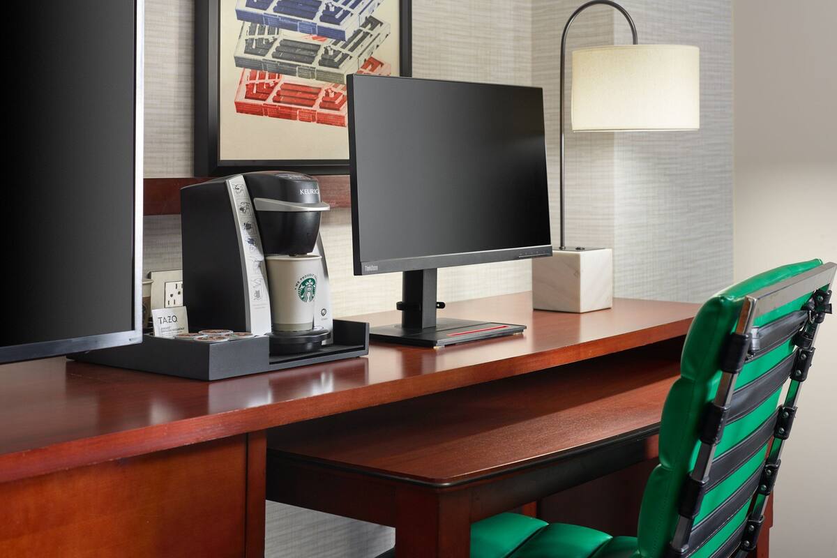 Un espace de travail dans un hôtel, équipé d’un ordinateur, d’une machine à café et d’une chaise.