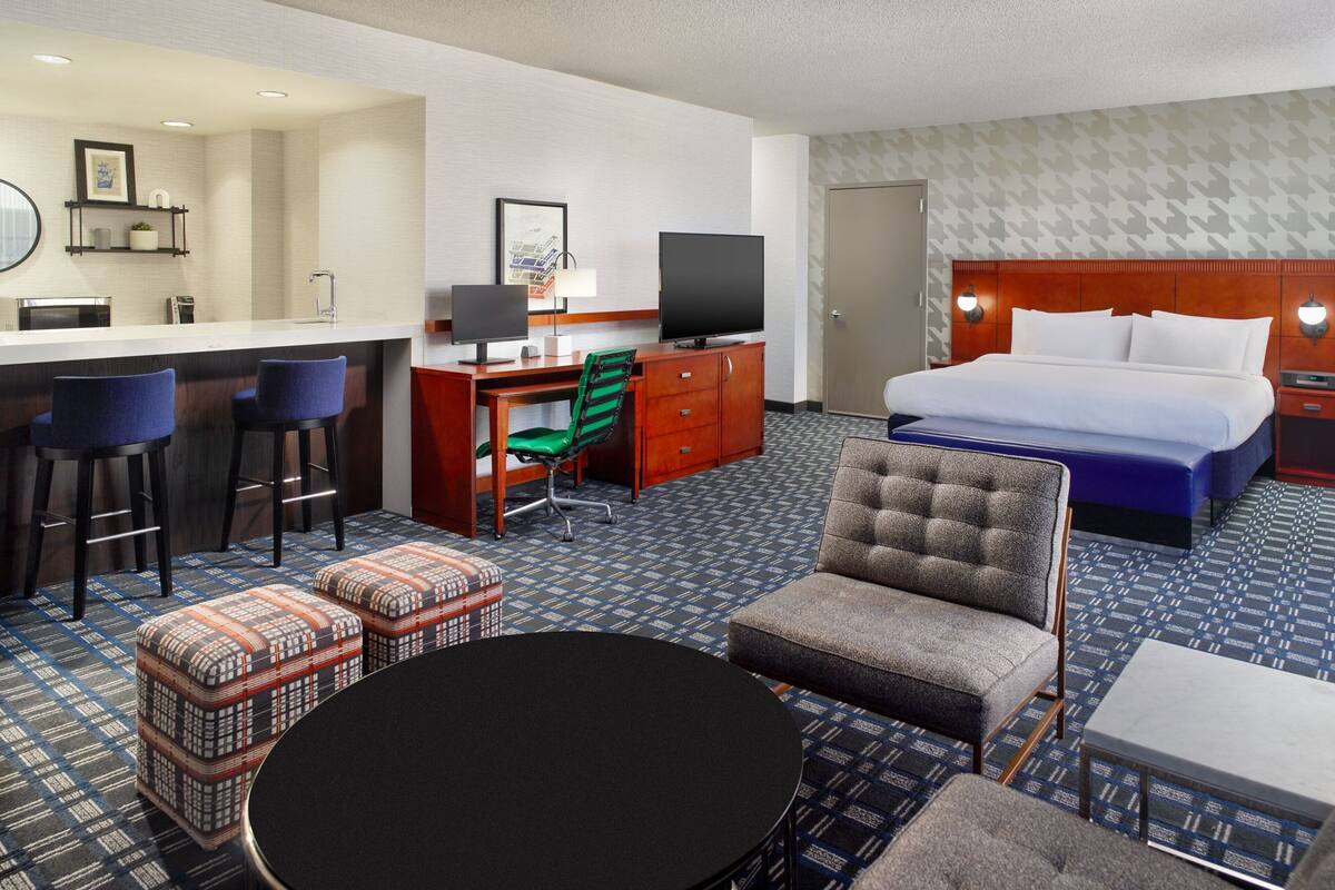 Une chambre d’hôtel comprenant un lit, un bureau avec un ordinateur, une chaise, une petite table et un coin bar.