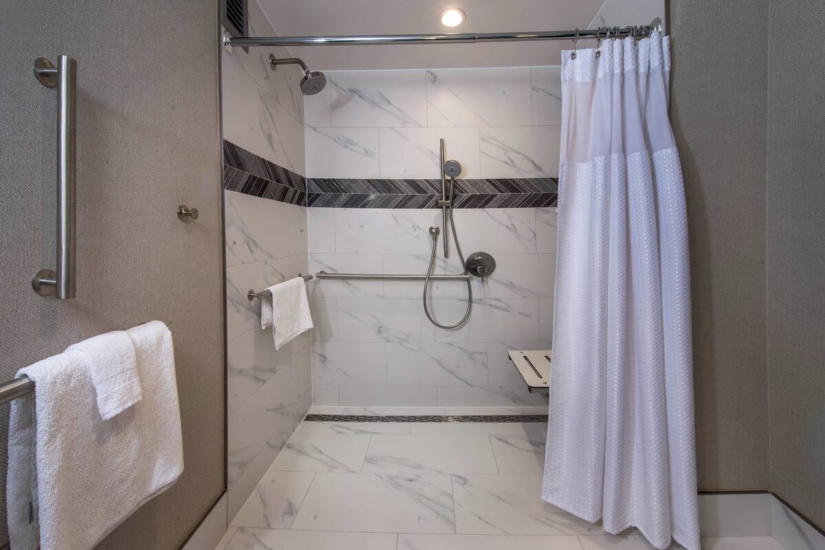 Une douche à l’italienne avec une porte en verre, une barre d’appui, un pommeau de douche et un porte-serviettes avec une serviette blanche.