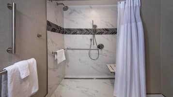 A walk-in shower with a glass door, a handrail, a showerhead, and a towel rack with a white towel.