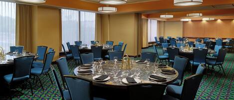 A conference room with round tables, blue chairs, and chandeliers.
